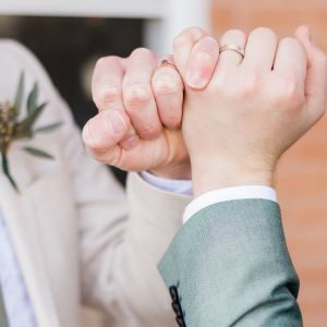 Two hands,
each wearing a wedding ring, with little fingers
entwined in a pinky promise