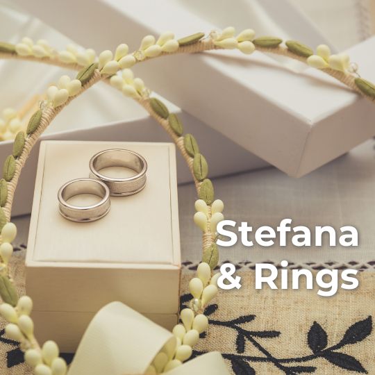 Two
wax orange blossom stefana (Greek wedding Crowns)
with a pair of silver wedding rings on a white
ring box