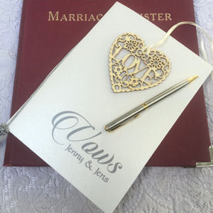 Vows booklet on a Marriage Register with a
silver and gold pen and a filigree wooden heart