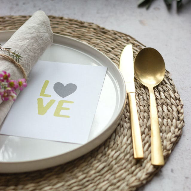 Wedding Reception place
setting. Rush mat. Gold knife and spoon. Rolled
napkin in napkin ring. Closed menu on plate with
heart and the word love printed on it